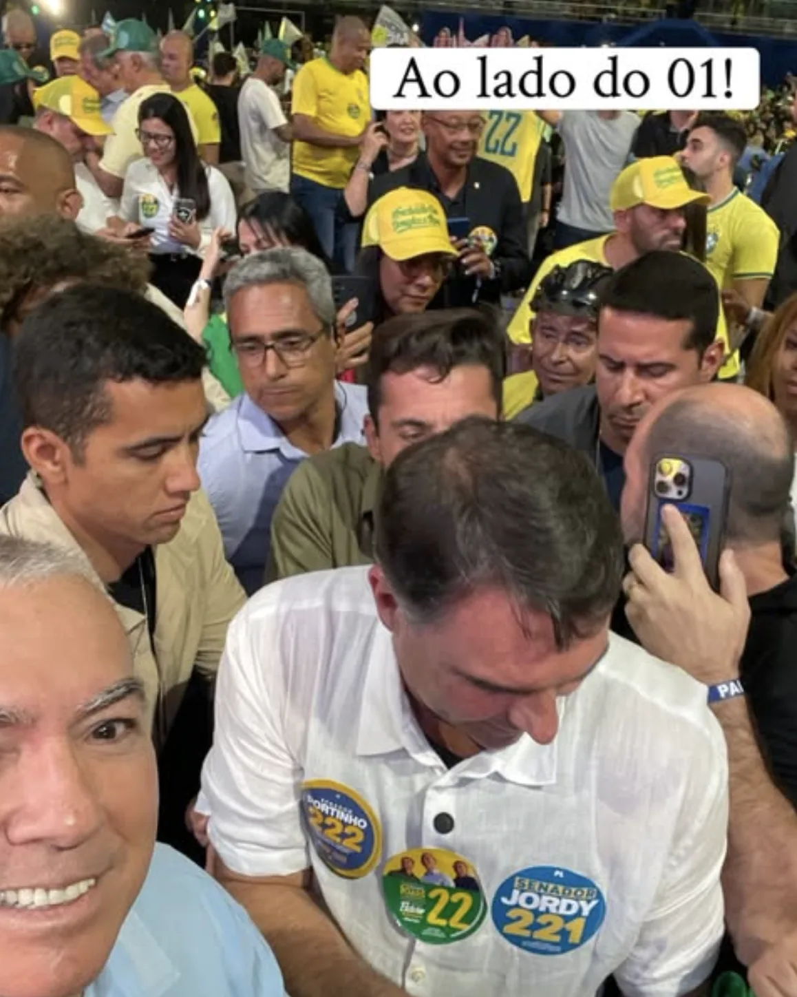 Paulo Bastos em selfie ao lado de Flávio Bolsonaro em evento de campanha, cercado por apoiadores